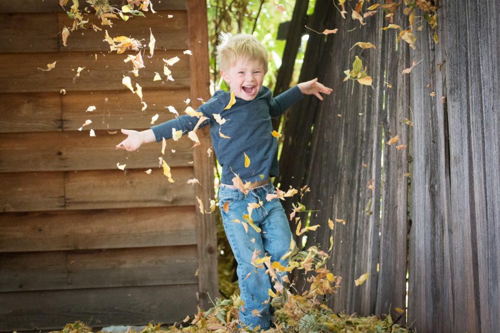 boy jumping in pile of leaves